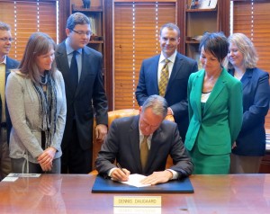 Governor Dennis Daugaard signs House Bill 1234 with Pierre bureaucrats watching and smiling.